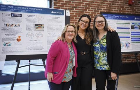 Three women stand togehter with arms around each other in front of poster presentations smiling.