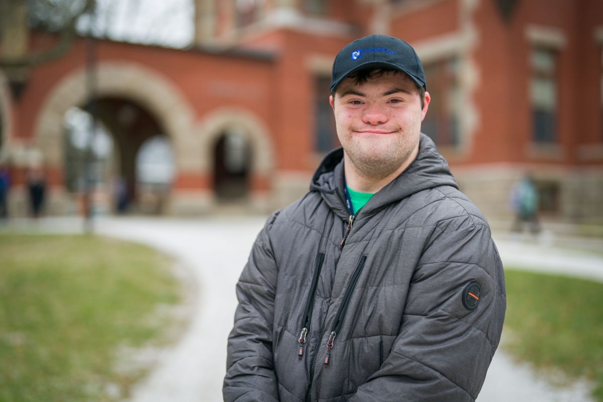 Andrew Strzykalski is a UNH-4U student wearing a UNH Hat and standing in front of Thompson Hall at UNH