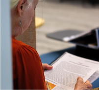 Over the shoulder view of a woman reading a printed spiral bound report.