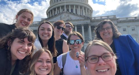 A group of happy excited people pose for a selfie in front of the US Capitol Building on a sunny day.