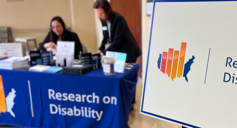 Event signage that says Research on Disability, with two women at the sign in table with the same branding in the background.
