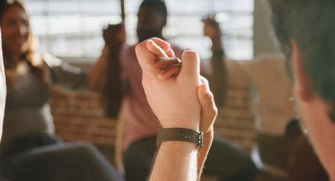 a diverse group of people gathered in mutual support, two clasp hands