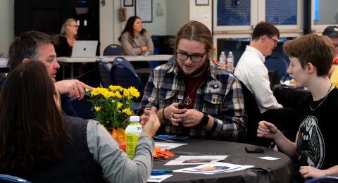 A group of people at an event sit together checking out an assistive eating tool.
