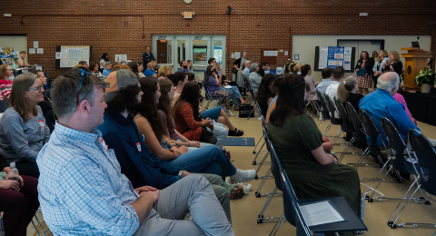 a diverse room full of people at an event look towards the speakers
