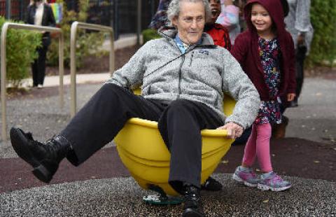 Temple Grandin sits in a bucket with kids on a playground.