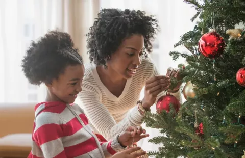 A Black woman and daughter decorate a Christmas tree.