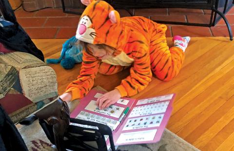 A young girl in a tiger costume works on an assignment via remote learning. 