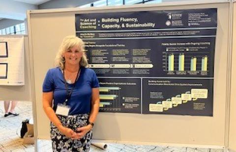 Kathy Francoeur stands in front of her poster "The Art and Science of Coaching: Building Fluency, Capacity, and Sustainability and Fostering Resilience to Support Our Most Vulnerable Youth"