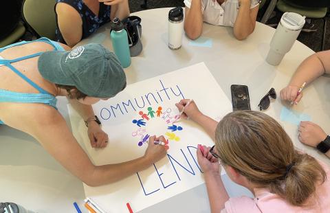 five LEND trainees gathered around a table drawing a poster that says Community LEND