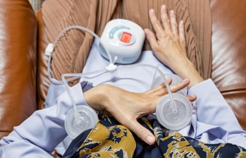 A woman sits in a comfortable chair as she uses a breast pump to express milk
