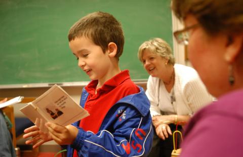 A young child looks at a flipbook while two teachers look on.