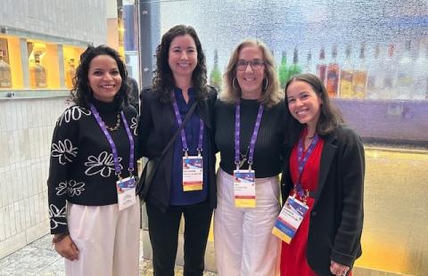 Four women in professional attire standing for a photo at a conference
