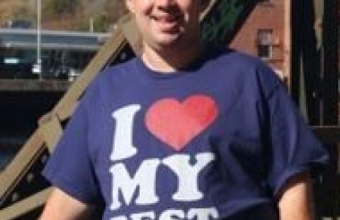 Alex standing outside while posing for the camera. He has a blue shirt that says “I love my best friend".