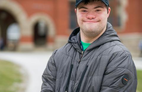 UNH-4U student Andrew Strzykalski  wearing a UNH Hat and standing in front of Thompson Hall at UNH