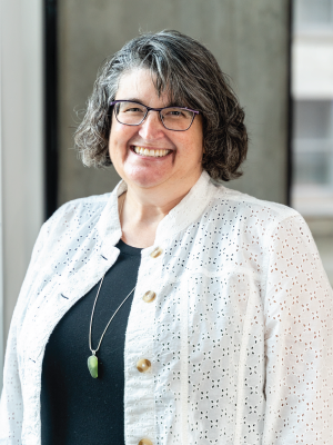 Stacy Driscoll is a woman wearing glasses with shoulder length curly salt and pepper hair