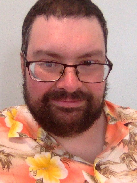 Abbott Philson is a man with glasses, short brown hair and a beard wearing a colorful hawaiian print shirt