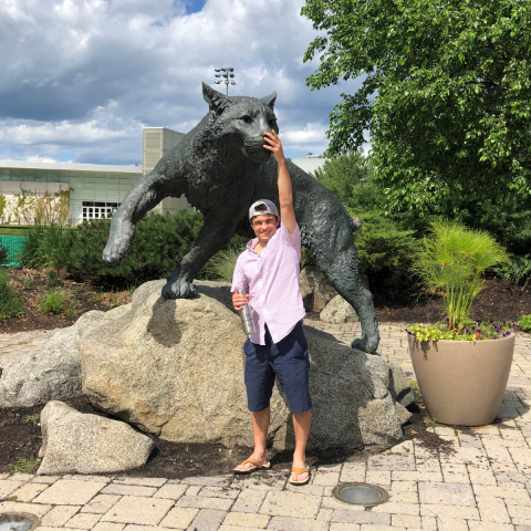 Garrett, a UNH-4U student standing in front of and touching the UNH wildcat statue's nose for luck