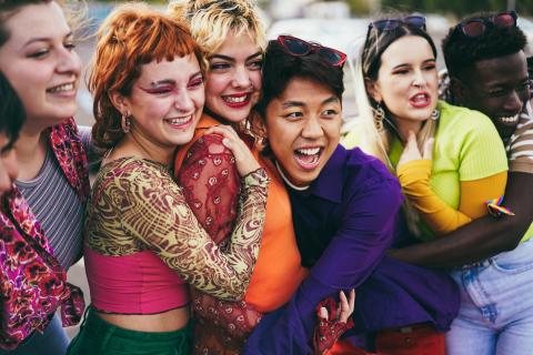 A group of teens of various races in various dress styles are huddled together and smiling.