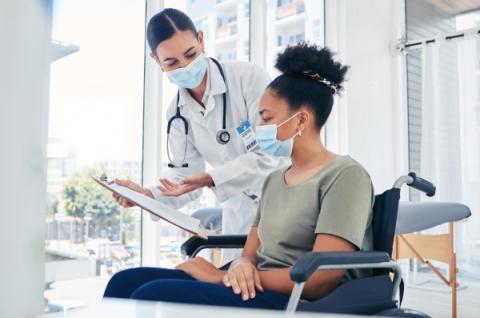 A doctor works with a patient in a wheelchair to fill out health screening paperwork