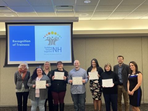 five graduates from Building Futures Together (BFT) 3rd cohort stand smiling with BFT staff holding up their certificates of completion in front of a screen saying Recognition of Trainees