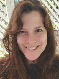 Jaime is a woman with wavy brown hair, outside pictured in front of white garden lattice work