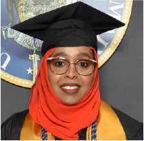 Fozia Robleh is a woman wearing glasses and a graduation cap over a hijab head scarf and graduation robes with a yellow scarf/trim for high honors