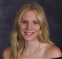 Klarissa Wankel is a woman with wavy blond hair, pictured in a formal portrait setting wearing a dark off the shoulder blouse and gold necklace.