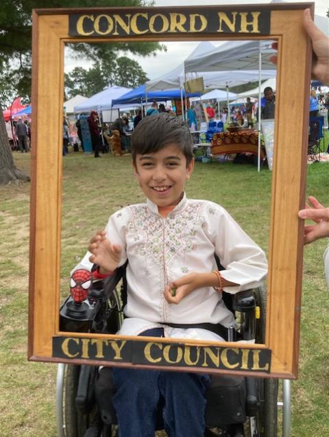 Bohdi smiles as someone off-camera holds an empty picture frame in front of him that reads "Concord, NH" at the top and "City Council" at the bottom.