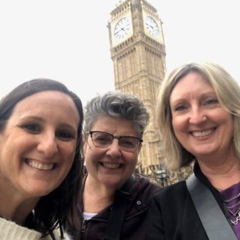 three women huddle together smiling in front of the Big Ben clocktower