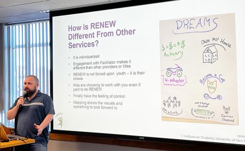 A white man in his thirties speaks into a microphone in a conference room, next to him on a big screen is a slide reading What Makes RENEW Different from Other Services?