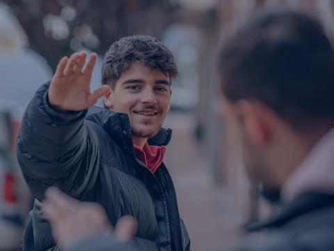 a young Latino person wearing a jacket waves to his friend on the street