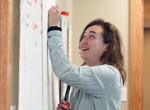 a smiling RENEW Facilitator writes on flipchart paper with an orange marker