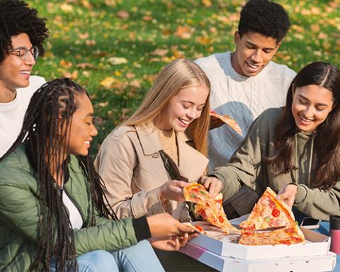 diverse youth sharing pizza outside on a sunny day