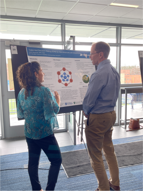 A woman and man are standing in front of a LEND poster about Supported Decision Making, engaged in lively conversation.