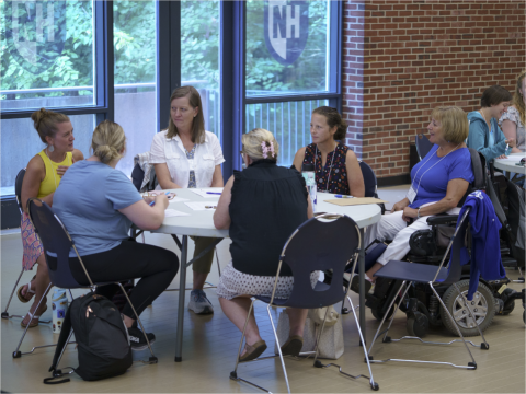 A group of LEND staff and trainees are sitting around a table engaged in conversation.