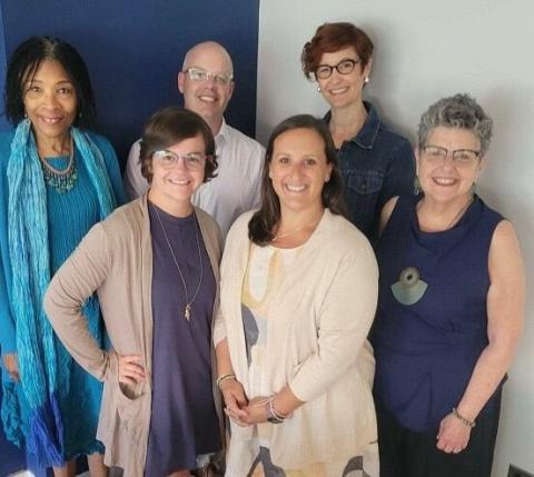 Six people in professional attire smiling for a group photo at a conference