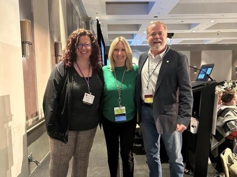 Three people in professional attire posing for a photo in a conference area