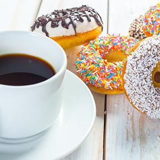 a cup of coffee on a saucer next to some donuts with varied sweet toppings