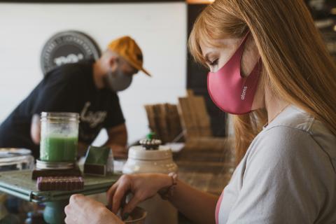 A cafe worker preparing someone's order and wearing a PPE mask