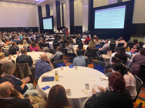 Hundreds of people at a conference focused on the speaker on the center stage.