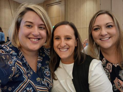 Three women in professional attire smiling and posing for a photo at a conference