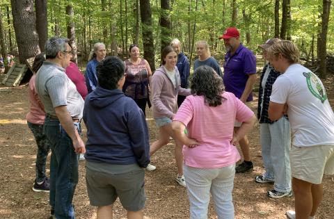 A group of adults participate in an activity, standing in a circle with one person walking around the center.
