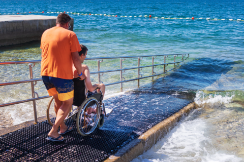 An example of what ABLE savings could enable: A man in a wheel chair and his companion go down an accessible ramp into the ocean at a beach