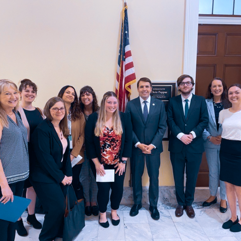 A group of 10 professionally dressed people pose happily in front of the door and plaque for Representative Chris Pappas' office.