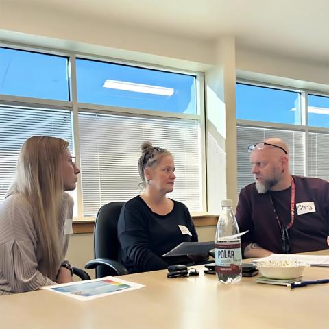 Two women and a man sitting at a table and talking in a sunny conference room