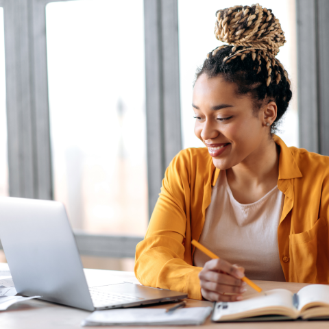 a young woman sits at a desk at home studying on her laptop