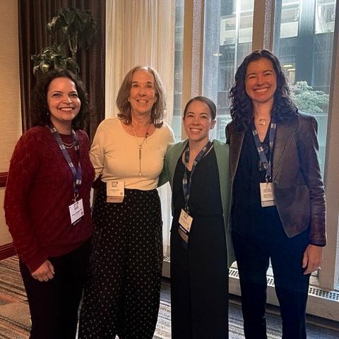 Four women in professional attire smiling for a group photo at a conference.