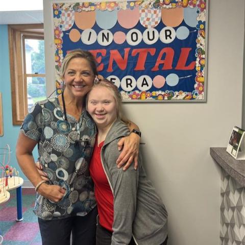 Two women pose together in front of sign that says, “In our dental era”.