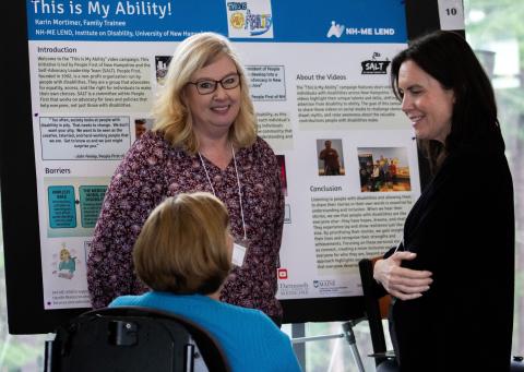 Three women stand talking in front of a poster that says This is My Ability!