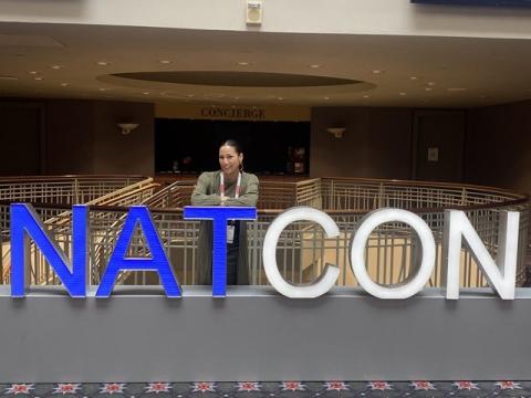A woman at a conference standing near large letters spelling NAT CON
